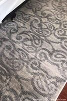 Photo of the rug showing the geometric pattern and some dust along the edges near furniture.