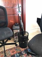 Photo showing Hoover Linx vacuum, two office chairs, black mesh waste basket, and stainless steel pedal trash bin against wooden door and white wall.