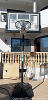 Full view of the portable Lifetime basketball hoop showing the base, pole, backboard and rim standing outdoors in front of a home.