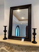 Front view of mirror flanked by two black candlestick holders on ornate beige surface