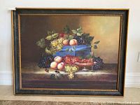 Full view of the framed oil painting depicting a still life with assorted fruits on table and blue container.