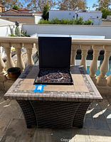 Front view of square wicker fire pit table with cover removed showing fire glass and burner