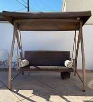 Front view of the entire outdoor loveseat swing under canopy with two pillows.