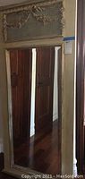 Full view of large rectangular wall mirror with cream colored carved frame reflecting wooden door.