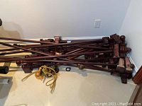 Multiple wooden drape rods piled on floor showing dark stained wood finish with various finials and square end brackets. Also shows several curtain tiebacks with gold and dark tassels/cords nearby.