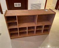 Photo showing the front view of wooden rolling occasional shelf with multiple compartments on the floor.