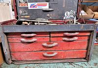 Front view of the vintage metal tool box chest showing red drawers with gray frame and handles that have wear and rust spots.