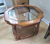 Front angle view of octagonal wood side table showing scalloped edges, glass top, bottom wood shelf, and turned legs.