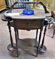 Front view of antique mahogany smoking stand showing the main body, drawer, and top surface with blue glass ashtray and metal strike zone.