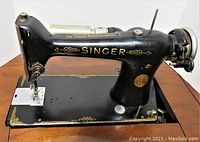 Close up of the black Singer sewing machine with gold detailing on the base and arm, showing brand name and machine details.