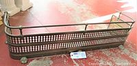 Full length view of the antique brass fireplace bumper on a red floor showing claw feet and pierced decorative panel