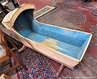 Angle view of the antique pine wood baby/doll rocking cradle showing blue interior paint and natural wood exterior with curved rockers