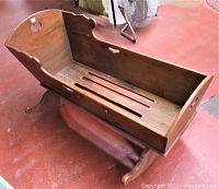 Side angled view of the wooden rocking cradle showing overall shape, base rockers, and brass handle on side.
