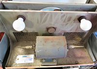 Front view of vintage Dayton electric polisher buffer grinder mounted on metal base with two light bulbs and cone polishing tips on motor shaft ends, powered off.