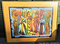 Large framed needlework textile art showing a folk art tribal scene with four female figures, floral patterns and a multicolor geometric design, framed in wood black and gold with a mustard mat