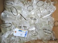 Large assorted group of clear glass drinking glasses with silver rims in a box with bubble wrap. Various shapes and sizes visible.