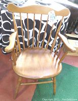Front view of the wooden Windsor chair showing the curved backrest with vertical spindles, curved armrests, and contoured seat.