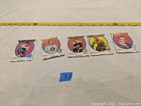 Five vintage hockey cards from the 1970s laid out side by side, featuring players from Canadiens, Penguins, Blackhawks, Canucks, and Flyers, with measuring tape showing size approximately 3.5 inches tall and 2.5 inches wide. Cards show wear, bends, and printing errors.