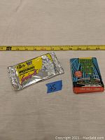 Two packs of collector cards placed flat with a measuring tape showing length. One pack is a silver foil WWF wrestler card series, the other a Teenage Mutant Ninja Turtles pack with detailed logo and character graphics.