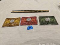 Three Silver Barber Quarters placed side by side, each in a protective display sleeve with decorative designs and year markings. A ruler is laid above for size reference.