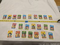 Photo showing multiple vintage hockey player cards with illustrated portraits lined up on a white background, tape measure indicating about 24 inches in total length.