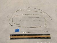 Six sterling silver necklaces laid flat next to a ruler showing approximate lengths and chain styles