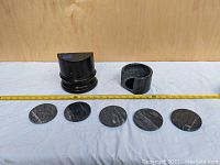View of two black marble semi-circular bookends and five round black marble coasters on a cloth with measuring tape.