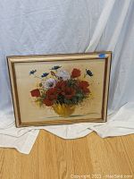 Full view of the oil on canvas still life painting showing floral arrangement with red, white, and blue flowers in a yellow vase in wood frame.