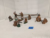 Wide view of nine lead toy soldiers in various military poses on white surface with visible wear on paint