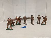 Front view of 8 painted lead toy soldiers on white background. Soldiers wear WWI helmets and uniforms, holding rifles in different poses.