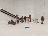 Full view of 9 hand-painted lead toy soldier figures arranged on white surface with a ruler for scale, including artillery cannon and flag bearer