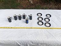Set of six black porcelain espresso mugs and six matching saucers arranged on white cloth with measuring tape indicating mug height.