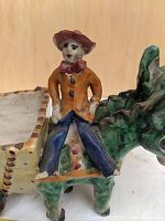 Close-up of the seated figurine on the two-headed donkey planter showing colorful attire and facial details.