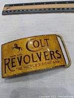 Front view of gold-tone Colt Revolvers belt buckle with size reference ruler on top