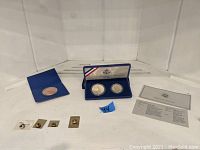 Overview of collection showing two coin sets in cases and four stamp pins.