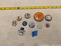 Photo showing full lot of 10 political and campaign buttons arranged on white surface with measuring tape for scale.