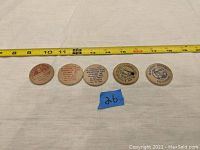 Five wooden nickels laid in a row with tape measure above showing approximate size and note number 26 in blue.