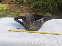 Front and side angle view of the old primitive hand-carved water bowl placed on a white cloth with yellow measuring tape showing approximate size of about 18 inches in length.