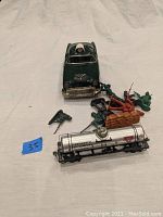 Overview photo showing the green vintage tin toy car, small metal train tanker, and scattered plastic soldier figures with accessories.