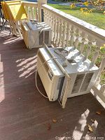 Two Kenmore AC window units placed side by side on a porch floor.