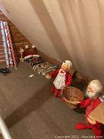 Wide shot showing Annalee Mr. and Mrs. Claus figures holding wicker basket, surrounded by boxes of holiday bulbs and rolls of wrapping paper.