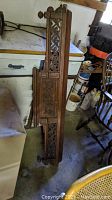Full view of the antique carved wooden trim piece leaning against furniture in a shed, showing overall length and design.