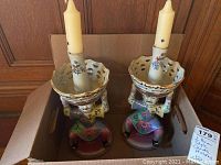 Pair of heavy ceramic Asian style candleholders with seated figures painted in multi-colored floral attire, each holding a scalloped dish with a candle on top.