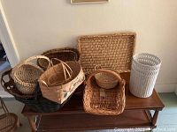 Seven baskets of different sizes and shapes on a wooden table against a plain white wall.