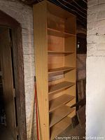 Side view of tall wooden bookshelf showing height and shelf spacing with brick wall background.