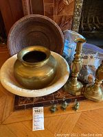 Photo showing brass vase nested inside a vintage beige wash basin, pair of brass candlesticks, carved wooden bowl behind, and four mouse-shaped metal place card holders lined up in front. Woven basket partially visible.
