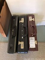 Five briefcases leaned against wall on floor, showing variation in color and wear