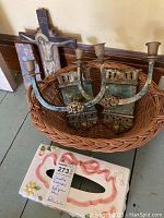 Pair of metal candle sconces in patina finish, wooden crosses, and ceramic tissue box cover shown in a wicker basket.