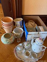 Group view of porcelain coffee set on tray, decorative vase, planters, cachepots, dried flower arrangement and box