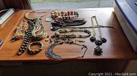 Overview of the lot laid on wooden table showing multiple necklaces, chains, bracelets, and the sterling brooch pin.